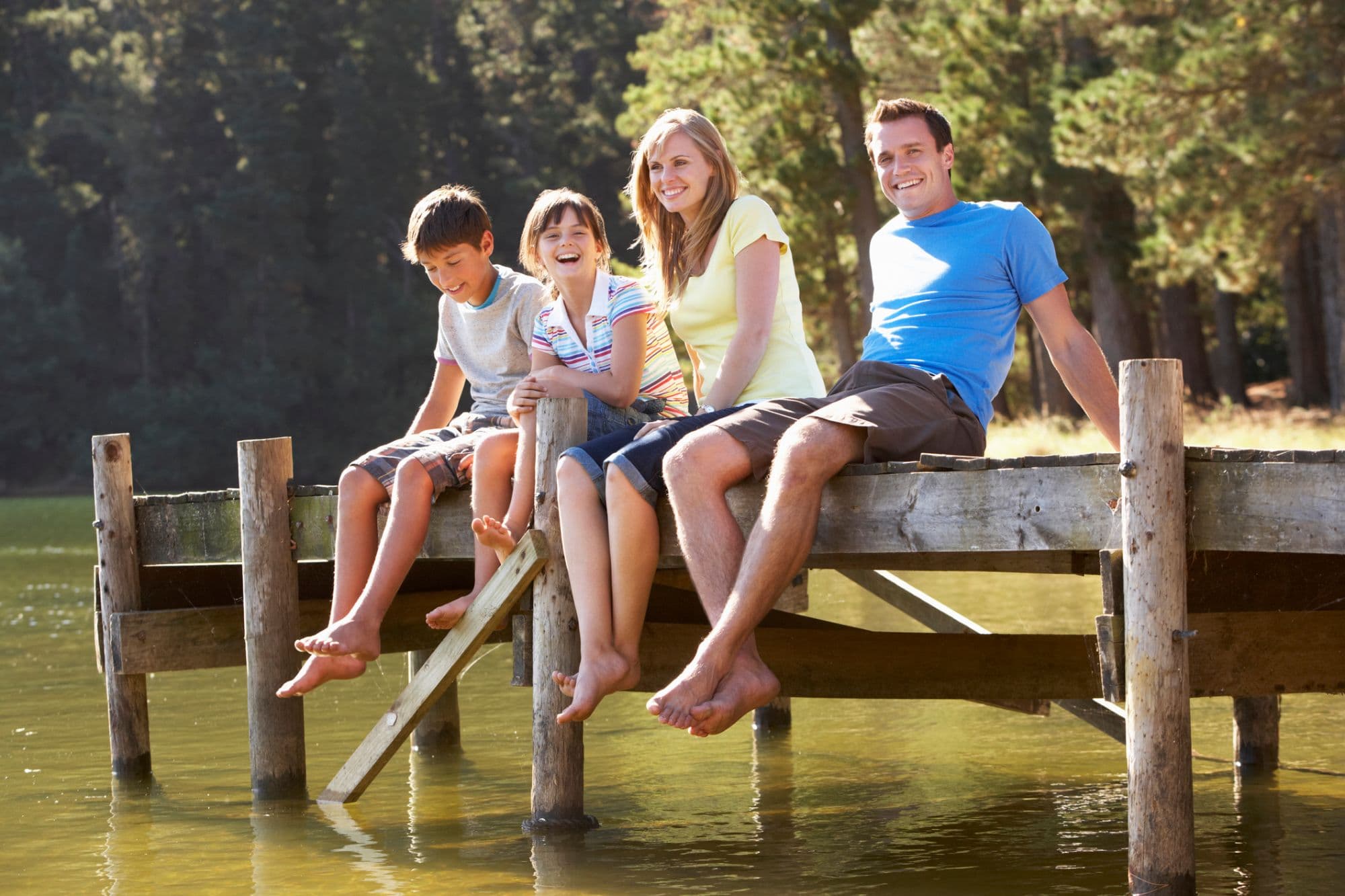A smiling family of four sitting together on a wooden dock over the water